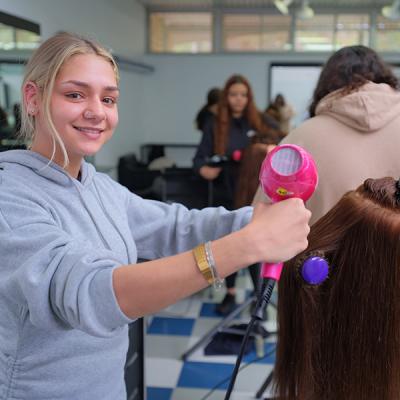 Decorative image - hairdressing student blow drying hair in the training salon (NMTAFE)