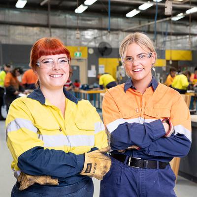 Decorative image - two female students smiling in PPE in a workshop (NMTAFE: Archer photography)
