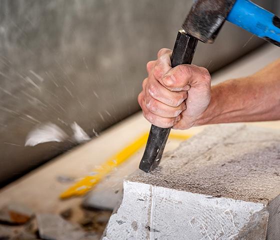 Decorative image- close up of a Stone Mason chiselling a grey stone block (iStock : CasarsaGuru)