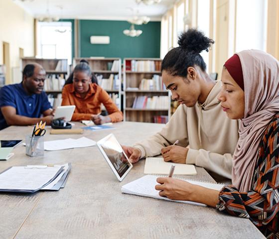 Four students viewing an iPad and taking notes with pen and paper