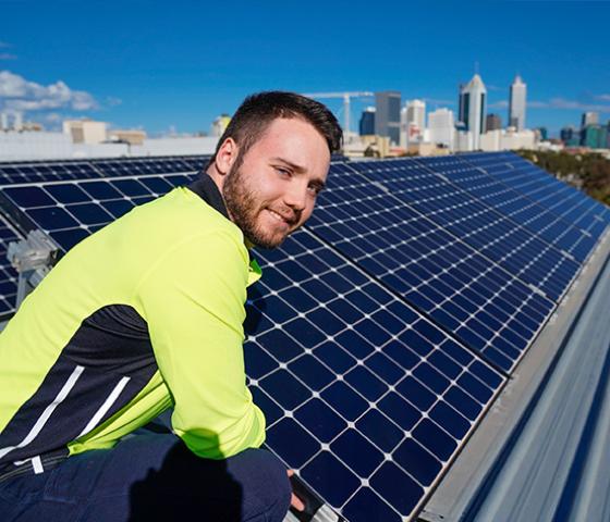 NMTFE student in front of PV system on roof of East Perth campus building