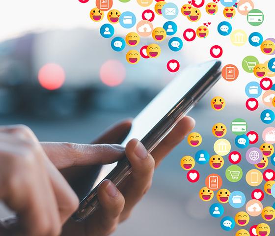 Hands holding a phone with colourful social media icons floating around it
