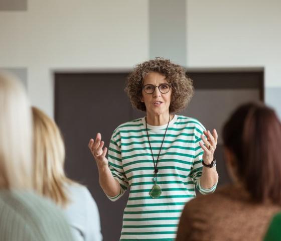 Woman at front of class talking with hands raised