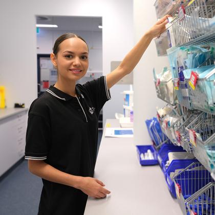 Student in a hospital storeroom reaching for supplies