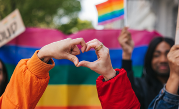 Hands making a love heart in front of a Pride flag